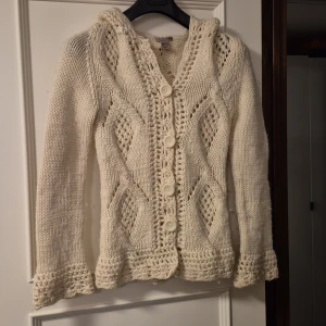 Vit stickad kofta med huva från H&M i ull - Supermysig vit stickad kofta från H&M med huva och stora knappar framtill. Snyggt stickad mönster vid ärmslut och nederkant samt ett öppet stickmönster som ger en cool look. Perfekt för lager-på-lager under hösten och vintern. 100% ull!