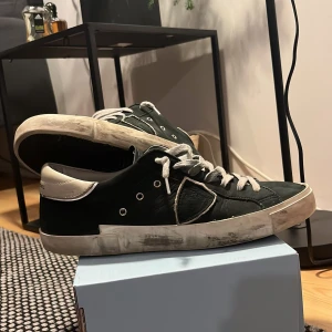 Philippe Model svarta sneakers i skinn - Svarta Philippe Model sneakers i skinn med vita detaljer och vit sula. Klassisk låg modell med snörning och rund tå. Snygg kontrast mellan svart och vitt, samt diskret logga på sidan och hälen. Perfekta för en stilren och avslappnad look. De är i fint skick, skriv vid frågor pris kan diskuteras.