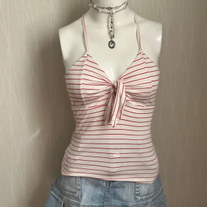 Randig vit och röd linnetopp med knyt - Säljer en söt linnetopp med tunna axelband och knyt framtill. Toppen är vit med smala röda ränder och har en croppad passform. Perfekt för sommaren och enkel att matcha med jeans eller kjol. Materialet känns mjukt och lätt.