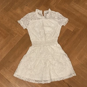 Vit spetsklänning med kort ärm - Superfin vit kortklänning från Cubus i spets med korta ärmar och markerad midja. Klänningen har rund halsringning och vackra spetsdetaljer över hela plagget. Perfekt för sommarens alla tillfällen!