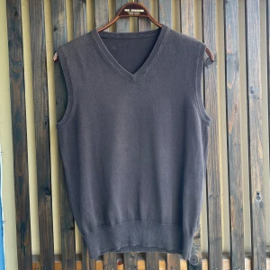 Brun stickad väst - En stilren brun stickad väst med v-ringad hals och ribbade kanter. Perfekt att bära över en skjorta eller t-shirt för en clean look. Västen har en klassisk passform och är helt enfärgad utan mönster eller detaljer.