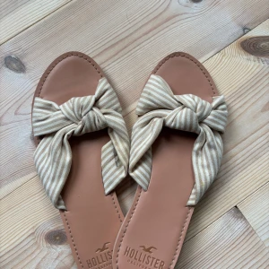 Randiga sandaler med rosett från Hollister - Säljer nu mina jättefina Hollister Sandaler i storlek 37. Säljer på grund av att de är för stora. De är inprincip helt nya och därmed i jättefint skick.   Säljes för 150kr Postar fort efter köp!