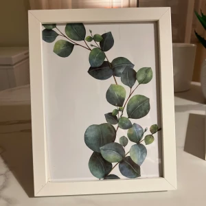 Vit fotoram med botaniskt motiv - Stilren vit fotoram med botaniskt bladmotiv.  Något slitage syns i hörnen, men i gott skick. Passar både stående och liggande placering.