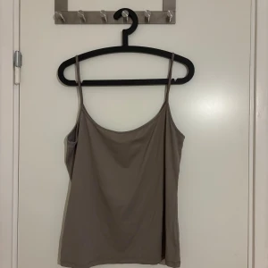 Beige linnetopp med smala axelband - Säljer en enkel och stilren beige linnetopp med smala axelband. Toppen har en mjuk och följsam passform, perfekt för att styla med jeans eller kjol. Materialet känns lätt och bekvämt mot huden. Snygg att bära både ensam eller under en skjorta. Använd bara 2 gånger.