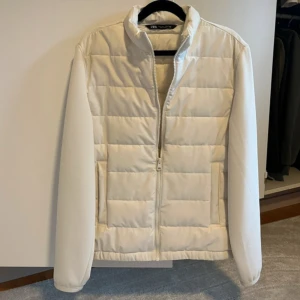 Vit pufferjacka från Zara, storlek S - Snygg vit pufferjacka från Zara i storlek S. Jackan har quiltad design, hög krage och dragkedja framtill. Perfekt för kyliga dagar och ger en clean look. Tillverkad i syntetmaterial och polyester för lätt och bekväm känsla.
