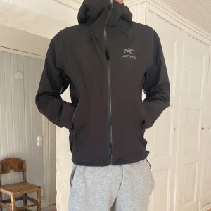Svart vindjacka (Helt ny) - (Moddelen är 183)Säljer en svart vindjacka från Arc'teryx med minimalistisk design, justerbar huva och vattentäta dragkedjor. Jackan är tillverkad i slitstark syntet och har två praktiska fickor framtill. Perfekt för dig som gillar stilren och funktionell outdoor. Kommer med tags!
