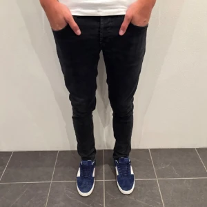 Svarta Nudie Jeans - Säljer ett par svarta jeans från Nudie Jeans. De har klassisk femficksdesign, svarta sömmar och en snygg läderpatch bak i midjan. Jeansen är tillverkade i stretchig bomull för skön passform och har en slim siluett som sitter slim hela vägen ner.