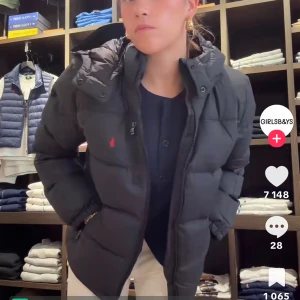 Svart pufferjacka från Ralph Lauren - Svart pufferjacka från Ralph Lauren med röd broderad logga på bröstet. Jackan har hög krage, dragkedja framtill och två fickor med dragkedja. Fylld för extra värme och har en klassisk, lite boxig passform. Perfekt för kalla dagar. Använd två gånger 