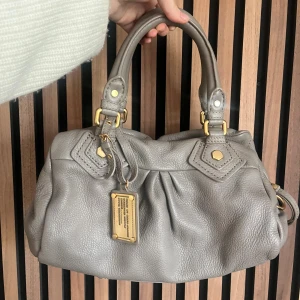 Marc Jacobs väska - grå/beige  - Marc Jacobs classic q baby groove med guldiga detaljer. Väskan är en varm grå/greiche. Axelremband ingår. Dustbqg ingår. Den är ca 30 cm bred och är i den lilla modellen. Mycket bra skick. Finns en slitning på väskans undersida, se bilder. Fler bilder finns och svarar gärna på frågor 🖤