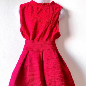 Set Röd ärmlös spet topp och kjol - Superfin röd kortklänning med ärmlös design och hög hals. Överdelen har ett vackert spetsmönster och kjolen är strukturerad med veck för extra volym. Perfekt för dig som vill sticka ut med en färgstark look.