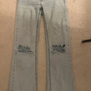 Ljusblå  jeans från Nelly - Ljusblå jeans från Nelly med slitna hål över knäna. med broderade detaljer på bakfickorna i rosa. Bootcut