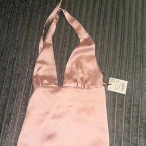 Ljusrosa halterneck klänning i satin - Helt ny Zara , ljusrosa topp satin med halterneck och djup v-ringning. Materialet är glansigt och ger en lyxig känsla. Perfekt för dig som vill sticka ut med en elegant och trendig look. Den är även backless.