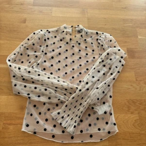 Prickig blus - Säljer en transparent blus i ljus beige med svarta prickar. Blusen har en knappstängning i nacken. 