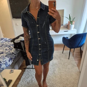 Jeansklänning S - Jeansklänning från 77thFLEA i storlek 34 men passar även mig som är en 36. Stretchigt material. Knappar framtill, korta ärmar och krage. 75% bomull 23% polyester 2% elastan. Använd vid två tillfällen, jättefint skick.