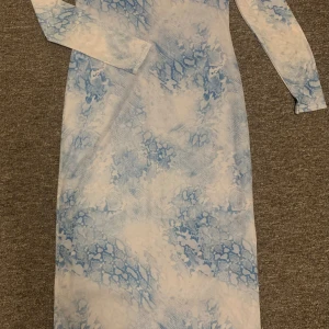 Blåvit långklänning Rita Ora x Primark - Säljer en långärmad långklänning från Rita Ora x Primark i storlek M. Klänningen har ett unikt blåvitt mönster som påminner om ormskinn och är tillverkad i ett stretchigt syntetmaterial. Rund halsringning och figurnära passform ger en modern vibe. Aldrig använd!