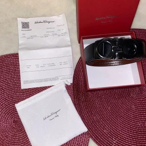 Salvatore Ferragamo svart/brunt skärp - Säljer ett lyxigt bälte från Salvatore Ferragamo i äkta skinn. Bältet är vändbart med ena sidan svart och andra sidan brun, och har ett ikoniskt, blankt svart spänne med Ferragamo-logga. Kommer med originalbox och duchbag. 