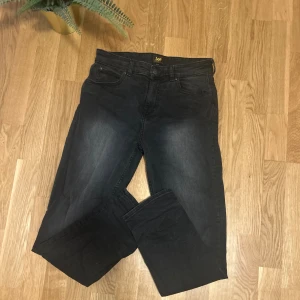Mörkgrå jeans från Lee - Säljer ett par mörksvarta jeans från Lee med snygg tvättad look. Klassisk modell med raka ben och normal passform. Perfekta för dig som gillar stilrena och bekväma jeans.