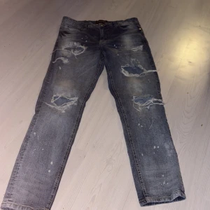 Distressed jeans Supply & Demand 34W - Säljer ett par blå jeans från Supply & Demand med slitna detaljer och hål på benen för en rå streetlook. Jeansen har normal passform, klassiska bakfickor och är tillverkade i denim. Perfekta för dig som gillar en edgy stil. Nypris 3000 säljer för halv priset   Kan gå ner lite vid snabb affär 