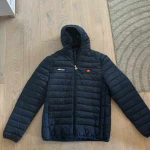 Mörkblå pufferjacka från Ellesse - Säljer en mörkblå pufferjacka från Ellesse med huva och dragkedja framtill. Jackan har quiltad design, Ellesse-logga på bröstet och är tillverkad i syntetmaterial. Perfekt för kyliga dagar och enkel att matcha med det mesta. Den är aldrig använd för att den passade inte mig! Det står storlek XL men det är mer som L! Nypris 1000kr 
