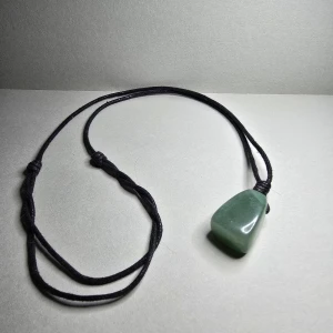 Halsband med grön sten och svart snöre - Unikt halsband med en polerad grön sten som hänge, uppträdd på ett svart justerbart snöre. Stenen har en mjukt triangulär form och ger en naturlig, stilren vibe. Perfekt för dig som gillar enkel men cool accessoar.