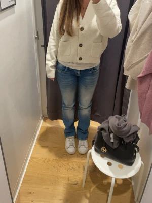 Beige kofta med knappar - Mysig beige kofta med v-ringning och stora bruna knappar framtill. Två fickor på magen och ribbade muddar vid ärmslut och nederkant. Perfekt för lager-på-lager och enkel att matcha med jeans eller kjol.