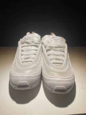 Nike Air Max 97 i beige och vitt - Nike Air Max 97 sneakers i beige och vitt med reflekterande detaljer. Klassisk vågig design, snörning och rund tå. Ovandel i syntet och textil, sula i gummi. Perfekta för dig som gillar en clean och modern look.