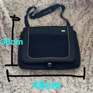 Svart datorväska från Pouch  - Säljer en stilren svart datorväska från Pouch med justerbar axelrem och praktisk dragkedja framtill. Väskan har ljusgrå kantdetaljer. Perfekt för att bära laptop och tillbehör. Snygg och funktionell design.