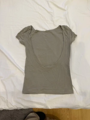 Olivegrön top och rygglös - Säljer en Olivegrön topp med korta ärmar och en öppen rygg från Gina tricot.Toppen är figurnära och gjord i mjukt bomullsmaterial, perfekt för att styla med jeans eller kjol. Enkel design utan mönster eller detaljer.