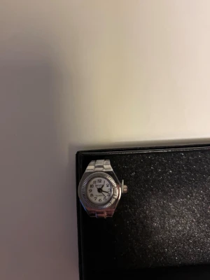 Silvrig ringklocka - En silvrig ring med inbyggd klocka. Passar till alla tillfällen, stilren och oanvänd. Justerbar storlek.