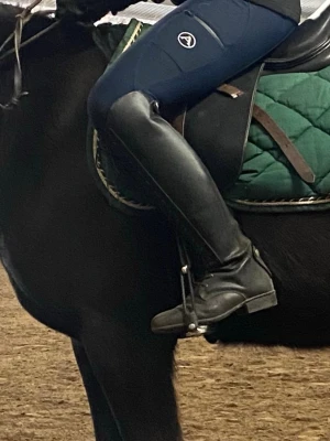 Svarta ridstövlar i skinn med snörning - Säljer ett par klassiska svarta ridstövlar i skinn med snörning framtill. De har rund tå, platt sula och går upp till knät. Perfekta för ridning och ger en snygg och stilren look i stallet. Nypris från Hööks cirka 2300, inte använda på länge men i ganska fint skick.