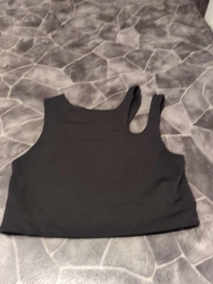 Svart  träningstopp från H&M Move - Säljer en svart träningstopp från H&M Move i storlek M. Toppen har en enkel och stilren design med breda axelband och ärmlös passform. Perfekt för träning eller chill dagar. Materialet är mjukt och stretchigt syntet som sitter skönt mot kroppen.