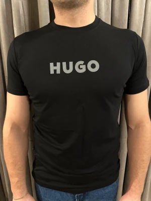 Svart HUGO t-shirt i bomull - Snygg svart t-shirt från HUGO med stor logga i grått framtill. Klassisk rund hals och korta ärmar. Tillverkad i mjuk bomull som sitter skönt och har en clean, modern look.