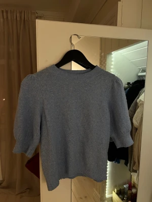 Ljusblå stickad kortärmadtröja från Vero Moda - Säljer en ljusblå stickad kortärmadtröja från Vero Moda i storlek XS. Tröjan har puffiga trekvartsärmar och ribbade muddar vid hals, ärmslut och nederkant. Använd kanske 2 gånger.