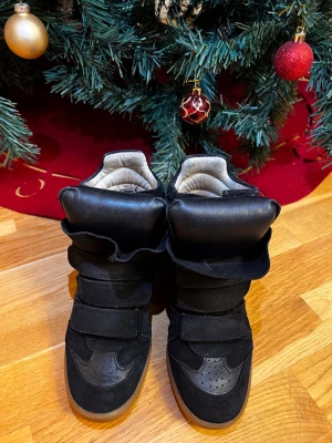 Svarta sneakers med kardborre och hög sula - Säljer ett par svarta sneakers med chunky design och högt skaft. Skorna har flera breda kardborreband, vadderad plös och detaljer i mocka och skinn. Yttersulan är i gummi och ger en cool kontrast. Perfekta för dig som gillar statement-skor och streetstyle.