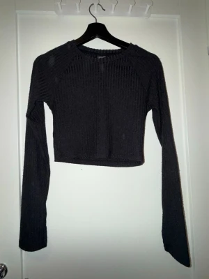 Svart croppad ribbad topp Gina Tricot - Säljer en svart croppad topp från Gina Tricot i storlek M. Toppen har lång ärm och är ribbad i materialet vilket ger en snygg struktur. Perfekt att styla med höga jeans eller kjol för en trendig look.