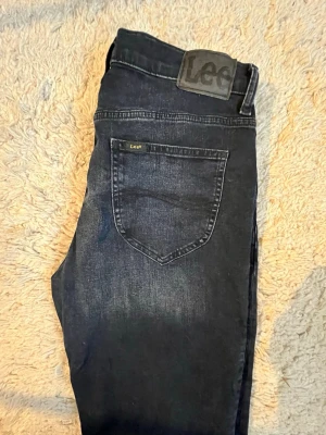 Mörkblå jeans Lee West - Snygga mörkblå (Below zero) Lee West jeans med klassisk femficksdesign och diskret Lee-logga på bakfickan. Storlek 31/30 Jeansen har en rak passform och är tillverkade i slitstarkt denimtyg. Perfekt för dig som gillar en enkel och stilren look. Köpt i nov 2025.