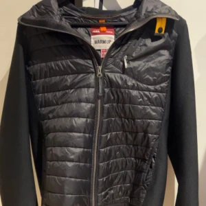 Svart Parajumper Cardigan Y-M/XS - Säljer denna då den är för liten för mig nästan helt ny utan några defekter. Snygg svart jacka från Parajumpers i storlek Y-M. Jackan har quiltade partier framtill och baktill, huva och dragkedja. Ärmarna är i ett stickat material och jackan har en gul detalj vid kragen. Perfekt för dig som vill ha en sportig och stilren look. Pris kan diskuteras vid en snabb affär. Passar dig som har XS eller är ca 170 cm lång.