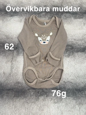 Beige randig body - Supersöt beige body med tunna ränder och ett broderat. Body har långa ärmar och praktiska övervikbara muddar. Perfekt för dig som gillar gulliga detaljer och mjuka material.🌸 Fint använt skick. Storlek 62