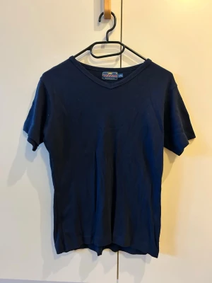 Mörkblå t-shirt från Vezzla Woman - Snygg mörkblå t-shirt från Vezzla Woman i storlek L/XL. Modellen har v-ringad hals och klassisk passform med korta ärmar. Materialet är mjuk bomull som känns skönt mot huden. Perfekt för dig som gillar enkel och stilren look.