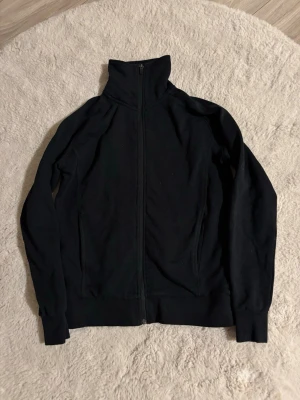 Svart tröja  från ID Identity med dragkedja  - Svart tröja med dragkedja från ID Identity i storlek M. Jackan har hög krage, hel dragkedja framtill och långa ärmar med muddar. Perfekt för kyliga dagar och enkel att matcha med andra plagg. 