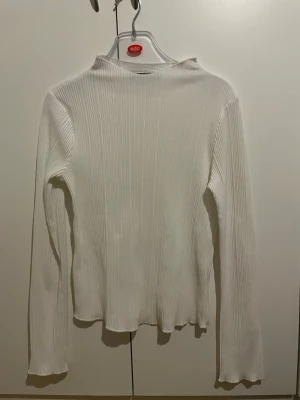 Vit ribbad långärmad topp BikBok - Säljer en vit långärmad topp från BikBok i storlek XS. Toppen är ribbad med en enkel, rak passform och har en mjuk, stretchig känsla. Perfekt att styla med jeans eller kjol för en clean look.