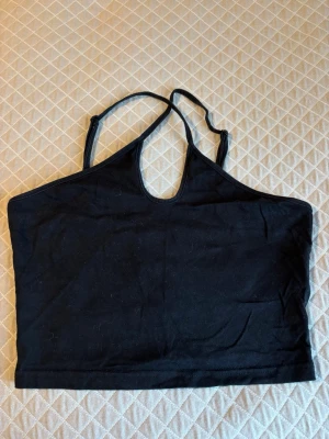Svart croppad linnetopp - Säljer en svart croppad linnetopp med tunna axelband och en liten cut-out framtill. Toppen har en enkel och clean design som passar perfekt till jeans eller kjol. Materialet känns mjukt och stretchigt, vilket gör den bekväm att bära hela dagen.