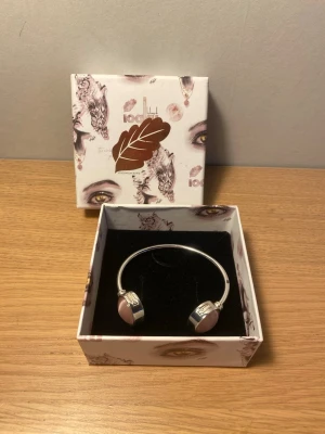 Ioaku armband - Ioaku armband, silver färgat och har rosa stenar. Använt en del och har ett jack ( se bild 5) men inga andra defekter. Ask medföljer. Hör av er vid frågor!💕