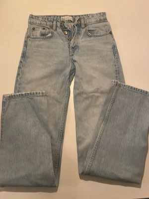 Ljusblå raka jeans från Zara - Säljer ett par ljusblå jeans från Zara med raka ben och klassisk femficksmodell. Jeansen har hög midja, knappgylf och är tillverkade i slitstarkt bomullstyg. Perfekta för en avslappnad och trendig look. Märke på baksida bortsprättat (endast sömmen från det syns)