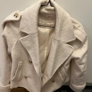 Vit teddyjacka från Nelly - Säljer en supermjuk och fluffig vit teddyjacka från Nelly. Jackan har breda slag, dubbelknäppning med silvriga knappar och två fickor framtill. Perfekt oversized look med coola axeldetaljer och uppvikta ärmslut. Fodrad insida för extra komfort.