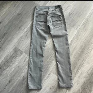 Grå jeans från Nudie Jeans, W30 L32 - Snygga grå jeans från Nudie Jeans med raka ben och klassiska bakfickor med vågig brodyr. Jeansen har normal passform och är tillverkade i mjukt denimtyg. Perfekta för dig som gillar stilrena och enkla jeans med en modern touch.