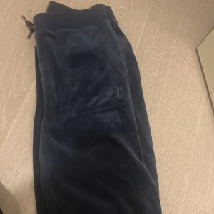 Mörkblå mjukisbyxor Juicy Couture XS - Mörkblå/ lila  mjukisbyxor från Juicy Couture i supermjuk velour med snörning i midjan och broderad JC-logga på fickan. Klassisk relaxed fit. Perfekta för chill dagar eller när du vill vara extra comfy.