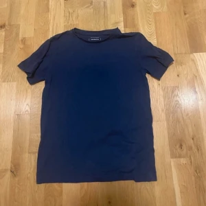 Mörkblå t-shirt från Calvin Klein - En stilren mörkblå t-shirt från Calvin Klein med klassisk rund hals och korta ärmar. Tillverkad i mjuk bomull för en skön känsla. Perfekt basic-plagg med diskret logga i nacken.