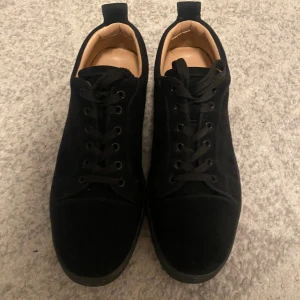 Louboutin skor - Snygga svarta sneakers från Christian Louboutin i mocka med klassisk rund tå och svart snörning. Insidan är beige och yttersulan har den ikoniska röda färgen med Louboutin-signatur. Perfekt för dig som vill sticka ut med stilrena detaljer. Priset kan diskuteras.