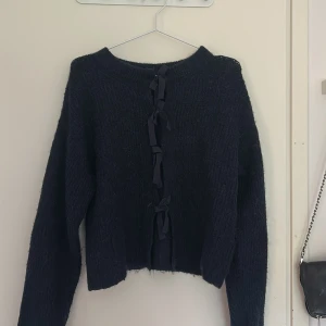 Svart stickad kofta med knyt från Gina Tricot - Mysig svart stickad kofta från Gina Tricot med långa ärmar och snygga knytband framtill. Perfekt för lager-på-lager och ger en cool touch till din outfit. Passar dig som gillar en lite loose och avslappnad stil.